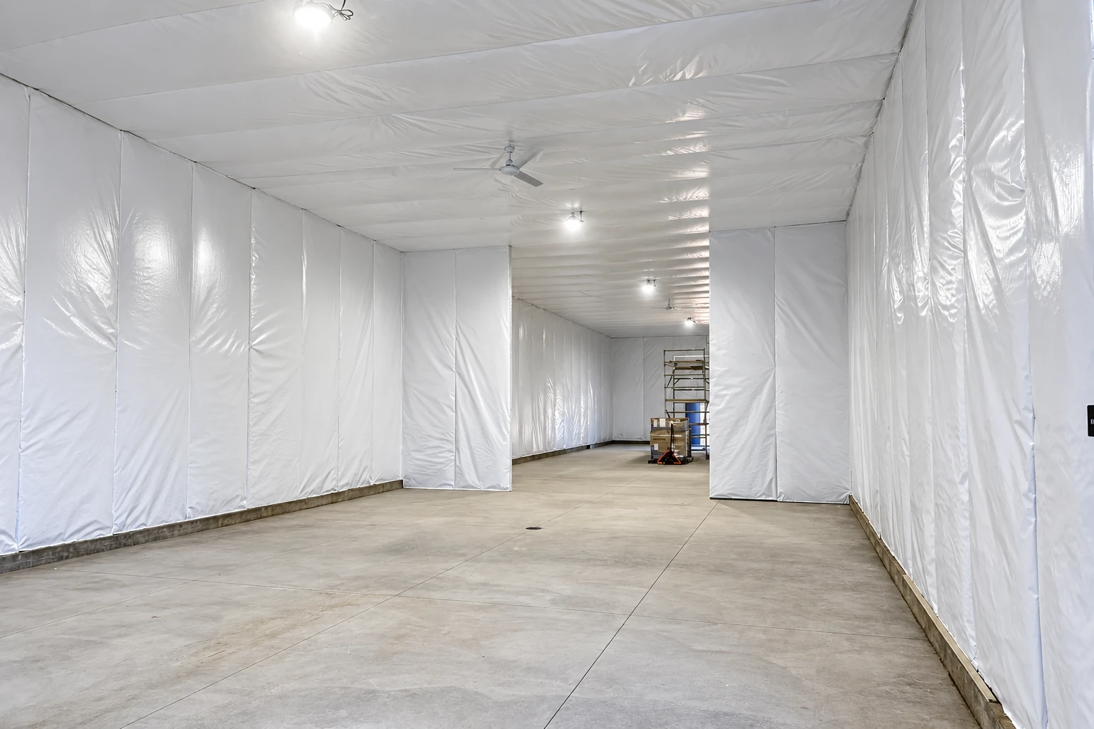 Commercial space lined with white plastic insulation and vapor barrier across the walls and ceiling, with a concrete floor.