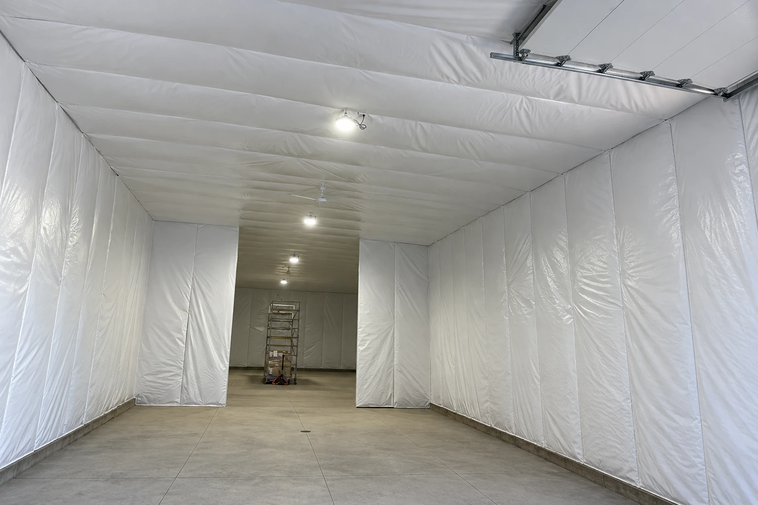Large room lined with white vapor barrier sheeting across the walls and ceiling, with a bare concrete floor.