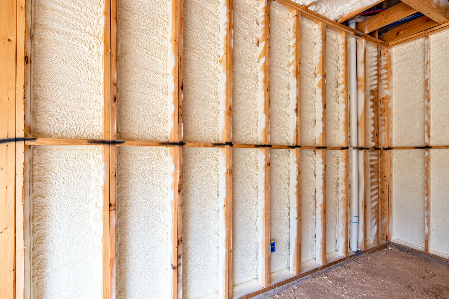 Spray foam fills the exposed wall cavities between wooden studs in an unfinished room.